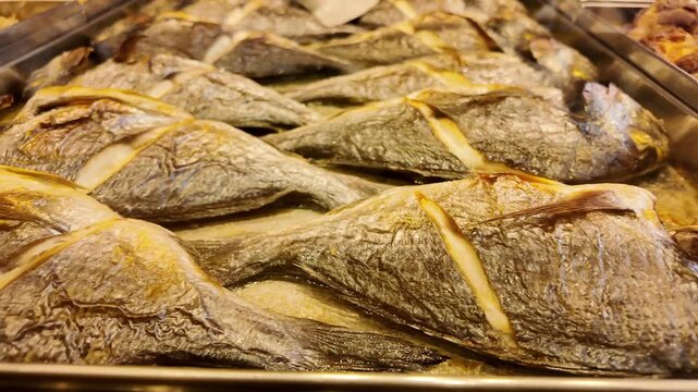 Freshly baked sea bream fish served on metal tray in buffet restaurant showcase