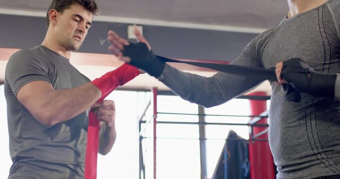 Diverse male sparring partners wrapping hands for sparring at boxing gym with red and black wraps