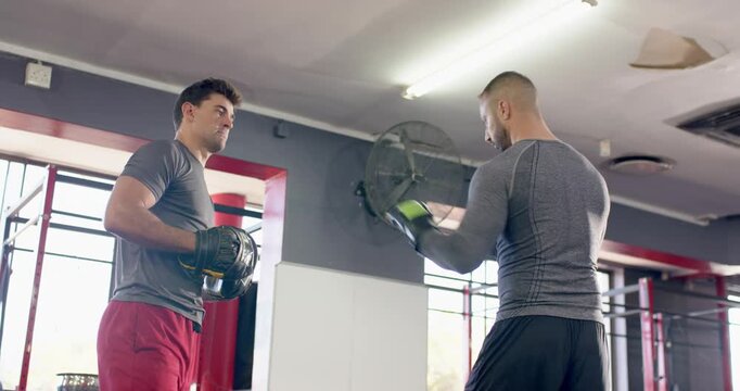 Diverse male trainer shifting mitts and trainee practicing combos in green gloves at boxing gym