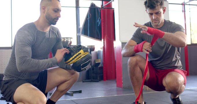 Diverse trainer and trainee pulling wraps winding around wrists, preparing for mitt work