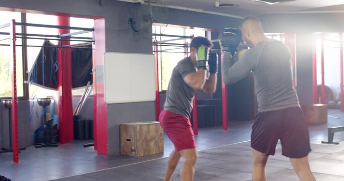 Diverse male coach and trainee cueing jab using mitts, throwing combos for technique in crossfit