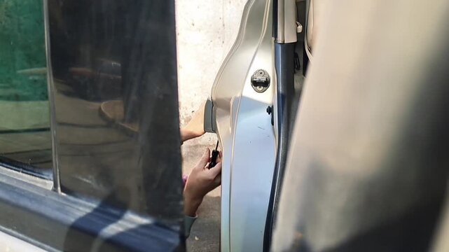 Repairing the rear wheel arch area on a silver vehicle. A person performs maintenance work on the lower part of the car body near the rear wheel well using a manual tool
