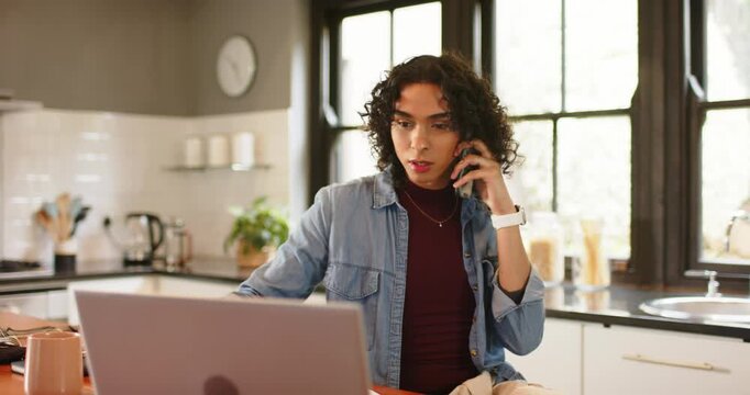 During phone call non-binary person picking up glasses, using laptop at kitchen island typing notes