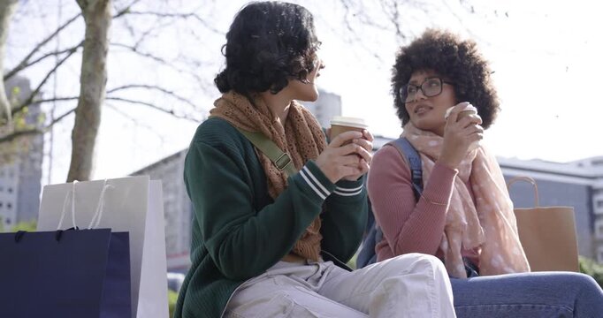 Diverse female friends tapping coffee cups to chat, sipping and pointing skyward on park bench