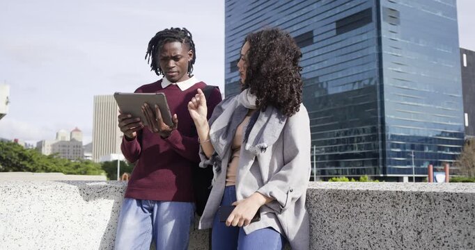 Diverse friends reading tablet content and scrolling on city terrace while discussing skyline view
