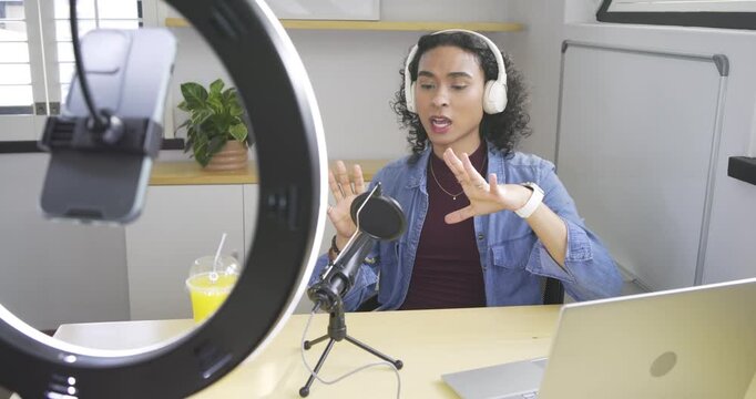 Settling at desk Asian non-binary creator adjusting microphone, explaining topic and pointing phone