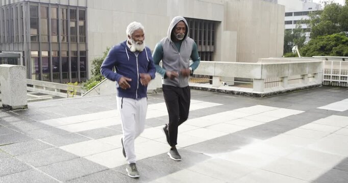 African American senior male friends checking watch then jogging across rooftop deck for workout