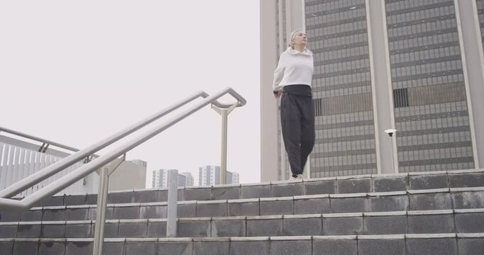 Woman initiating warmup descending stairs while senior woman ascending checking smartphone