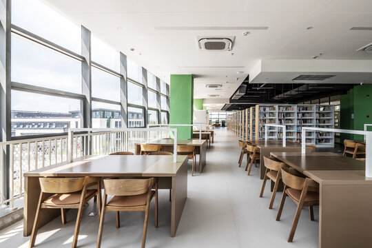 Modern library reading area with wooden tables chairs and bookshelves