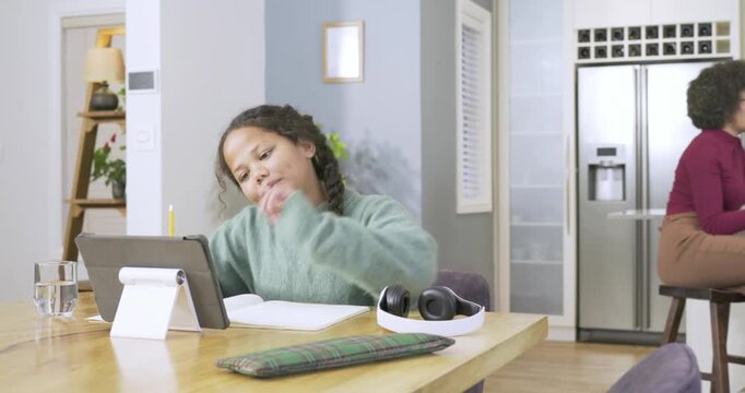 Girl pulling headphones, bopping head then writing notes and cheering at tablet at dining table