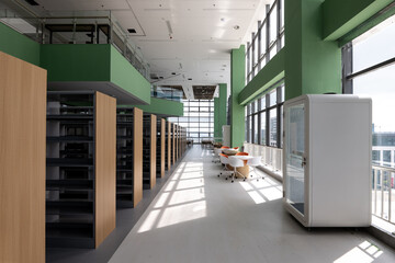 Fototapeta premium Modern library with green bookshelves, sunlit reading area and clean interior design