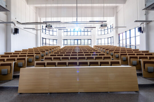Modern university lecture hall with empty tiered seating and wooden podium under bright natural light