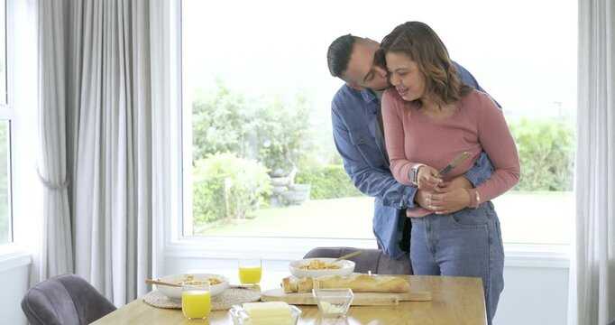 Diverse couple preparing breakfast at home slicing bread embracing twirling pasta and sipping juice