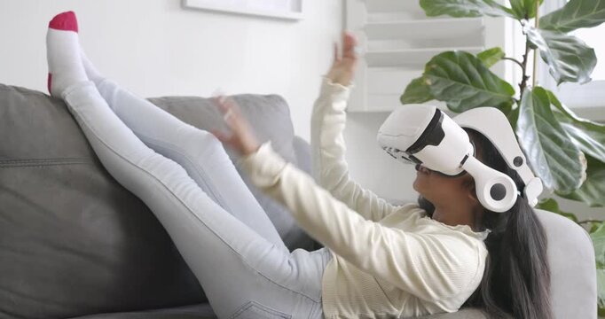 Bringing VR headset to eyes on gray sofa, child adjusting straps, exploring VR scene, copy space