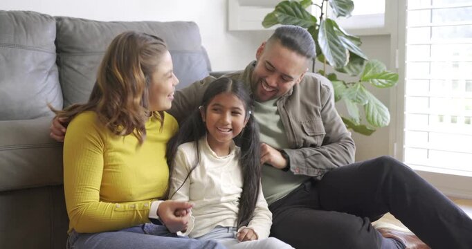 Family leaning in tickling daughter on grey sofa at home causing giggles and playful bonding