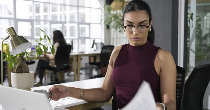 Hispanic woman picking up report scanning charts sipping coffee entering data on laptop, copy space