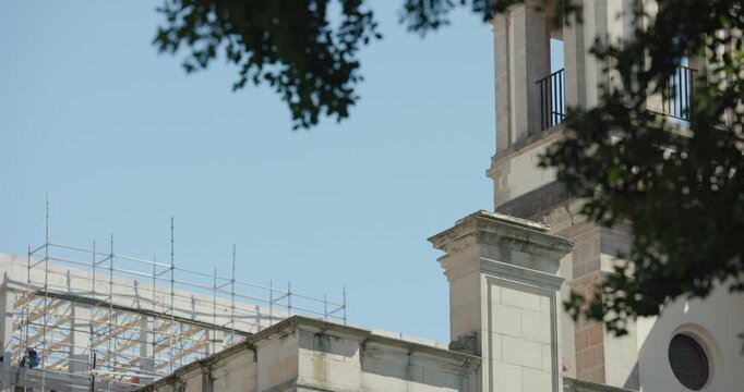 Light breeze is swaying branches while worker is repairing tower on scaffolding during renovation