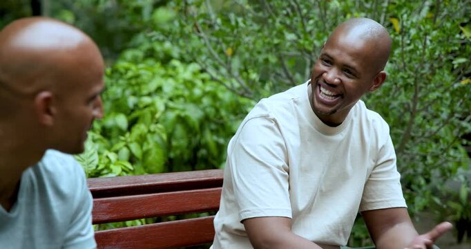 African American friends sitting on red bench, right man telling joke, cheering and bumping fists