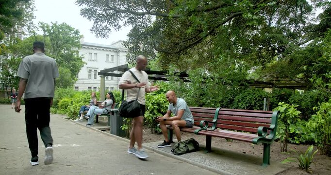 African American men on park bench arriving man placing bag chatting catching up, copy space