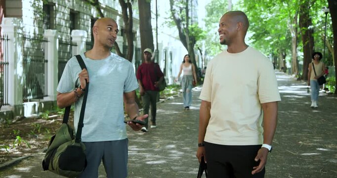 African American men walking path in activewear, left showing phone, right gesturing, sharing info