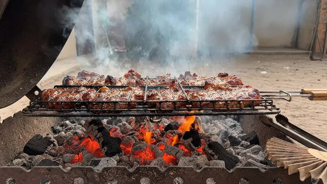 Traditional meat grilling on an outdoor charcoal barbecue with smoke rising during an indian eid al-adha celebration.