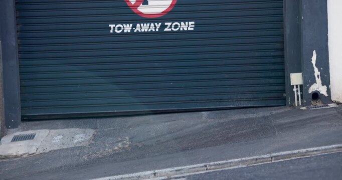 Diverse pedestrians after pause walking along sidewalk past shutter labeled TOW AWAY ZONE commuting