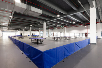 Naklejka premium Indoor sports hall with neatly arranged table tennis tables and blue barriers