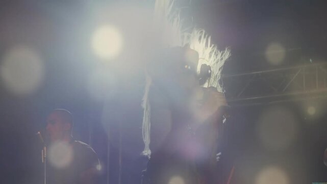 Lead singer whipping hair, with mic, singing, beat driving motion and lens flares overlaying singer
