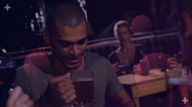 Man clinking glass in dim bar, camera pulling back, causing flares, drinking beer for hospitality