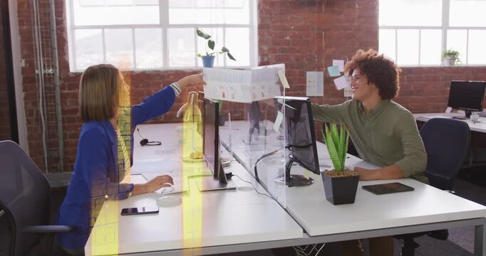 Vertical video: Extending man in green handing paper over clear divider to woman for review at desk