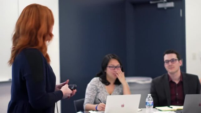 Charismatic smart-casual presenter lectures to diverse professionals taking notes on laptops in a modern, bright seminar room with soft bokeh background. Professional development concept