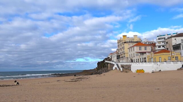Quiet sandy beach at Praia das Macas with Atlantic waves and traditional Portuguese houses under autumn clouds