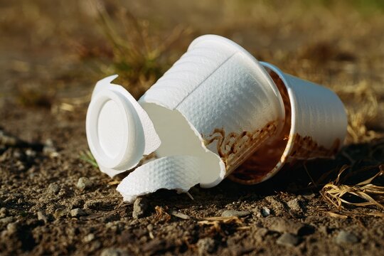Discarded styrofoam coffee cup with lid lying on the ground outdoors