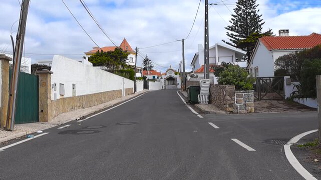 Quiet uphill street in Colares lined with white Portuguese houses red rooftops and soft coastal light.