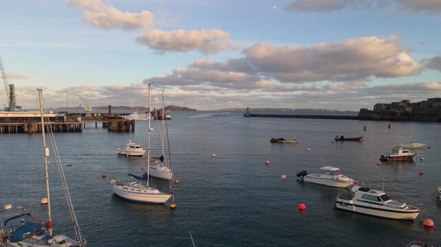 St Peter Port Harbour,Guernsey,low flight over outer harbour towards harbour entrance with Herm and Jethou beyond past Castle Cornet in late afternoon sun with calm waters and golden light