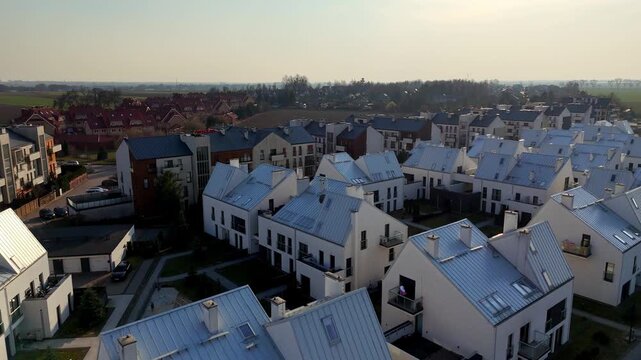 Aerial panorama of a modern residential estate with white terraced houses and gabled roofs. Drone view of contemporary suburban architecture, real estate development, and housing infrastructure in day