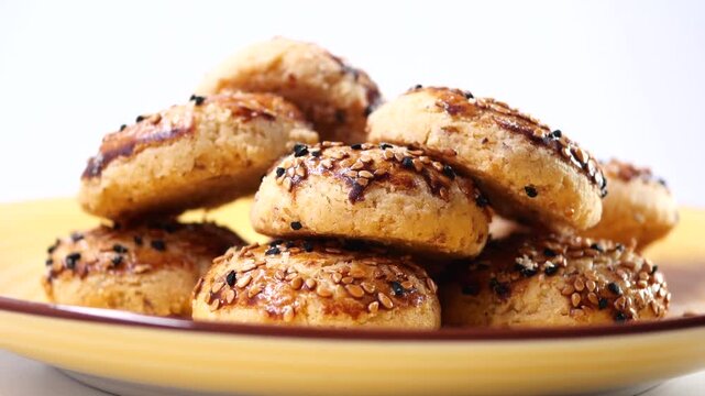 Freshly baked salty cookies with sesame and black cumin seeds rotating on yellow plate over white background