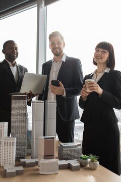 A diverse group of professionals stands in an office, reviewing architectural models and using technology