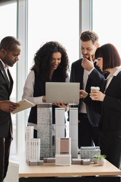 A diverse design team reviews a city scale model and digital plans around a laptop in a bright office