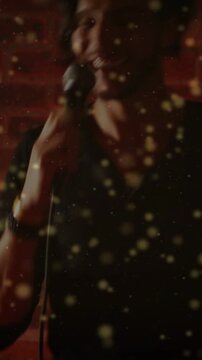 Singer lifting mic, leaning into mic, singing on stage, gold particles over him and brick wall