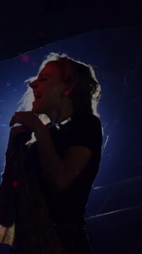 Vertical video: Female singer singing, leaning into mic on stage, backlight causing silhouette