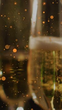 Vertical video: Rising bubbles urging champagne flutes moving center, specks drifting for warm glow