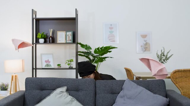 Asian Female Burglar Rummaging Through Living Room Behind a Sofa