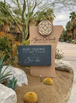 Palm Springs, Ca on November 22, 2025. The Agua Caliente Cultural Plaza and Museum Signage in Palm Springs, California. desert landscaping with palm trees, cacti, and boulders under a bright sky.