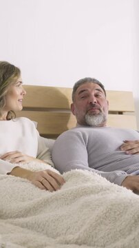 Vertical video: Leaping retriever entering frame, sparking couple talk on bed under fleece blanket