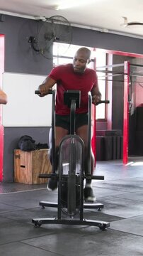 Vertical video: Pedaling steady, man in red shirt pushing harder on air bike at gym for cardio