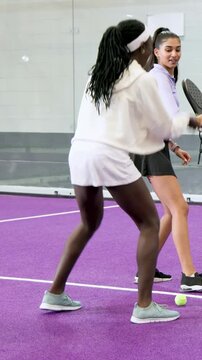 Vertical video: Holding balls, hoodie feeding lavender top with paddle training on glass court