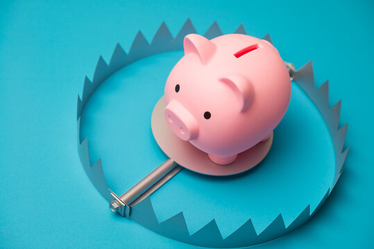 Piggy bank in trap on blue background. Financial scam or fraud, savings in danger, high interest rate loan, high risk investment, financial trap, untouchable savings, money literacy and so on concept.