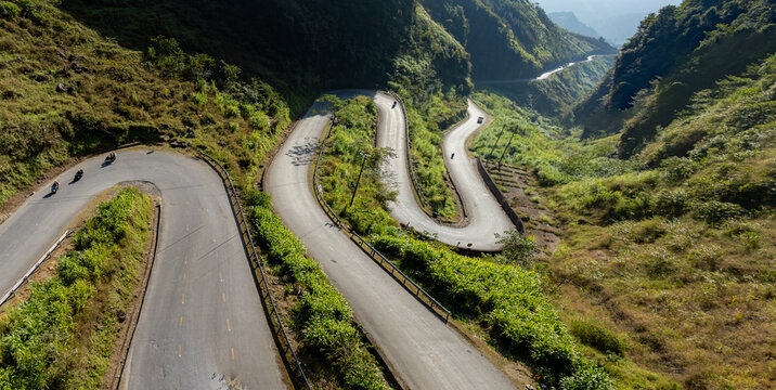 Motorcyclists navigate the winding mountain roads of Doc Tham Ma Pass, Dong Van, Ha Giang, Vietnam. The steep terrain and lush greenery make it a popular destination for adventure tourism.