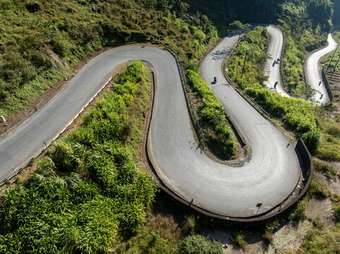 Motorcyclists navigate the winding mountain roads of Doc Tham Ma Pass, Dong Van, Ha Giang, Vietnam. The steep terrain and lush greenery make it a popular destination for adventure tourism.
